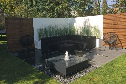 Moderner Gartenbrunnen auf der Terrasse zusammen mit Loungesesseln Loungeecke
